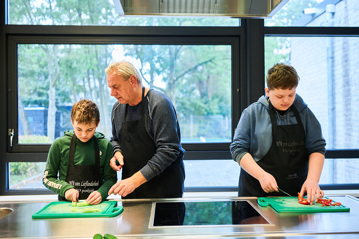 Twee vso-leerlingen en docent zijn bezig met snijwerk in kooklokaal.
