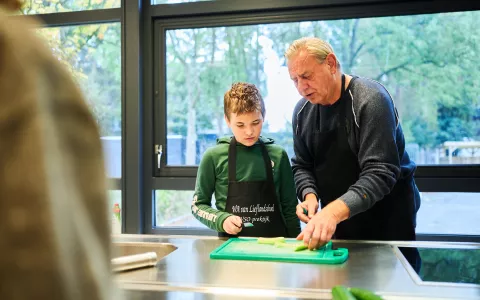 Leerling en docent zijn bezig met snijwerk in kooklokaal.