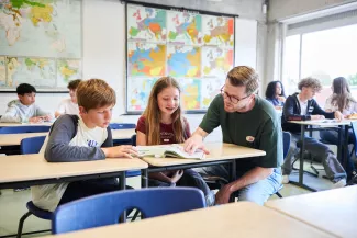 Docent kijkt mee met leerlingen in het aardrijkskundelokaal.