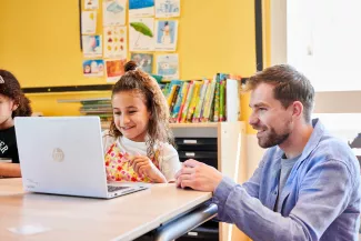 Leerling en meester werken samen in klaslokaal achter laptop.