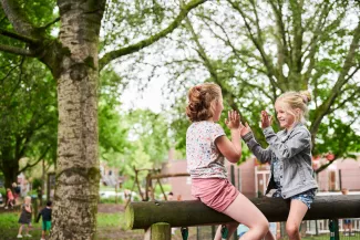 Twee leerlingen spelen buiten op houten balk.